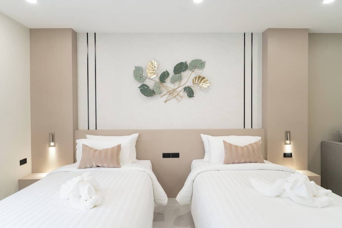 A hotel room with two beds, beige walls, a decorative wall piece, and bedside lamps.
