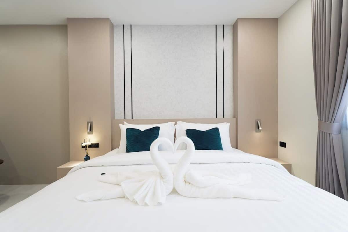 A hotel room with a large bed, two pillows, bedside tables, and a curtain.