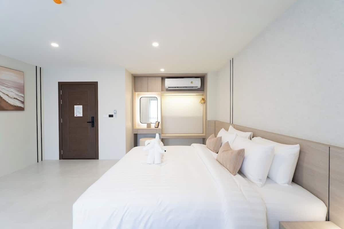 A modern hotel room with a large bed, a bedside table, a built-in air conditioning unit, and a door with a handle.