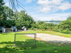 Een omheind sportveld met een doelpaleis, een klein tuinhuisje en een picknicktafel.