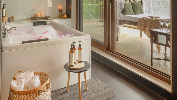 Uma casa de banho moderna com uma banheira grande, uma mesinha com produtos de higiene pessoal e vista para uma varanda com cama e cadeira suspensa.