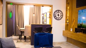 A modern living room with a blue sofa, a wooden reception desk, and a wall clock. - Luxury 3BR Ensuite Apartment 24/7 Power Fast WiFi Secure Estate Ikeja Lagos (Ikeja)