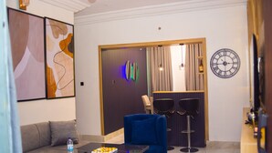 A modern living room with a sofa, a blue chair, a dining area with two chairs, a clock, and abstract wall art. - Luxury 3BR Ensuite Apartment 24/7 Power Fast WiFi Secure Estate Ikeja Lagos (Ikeja)