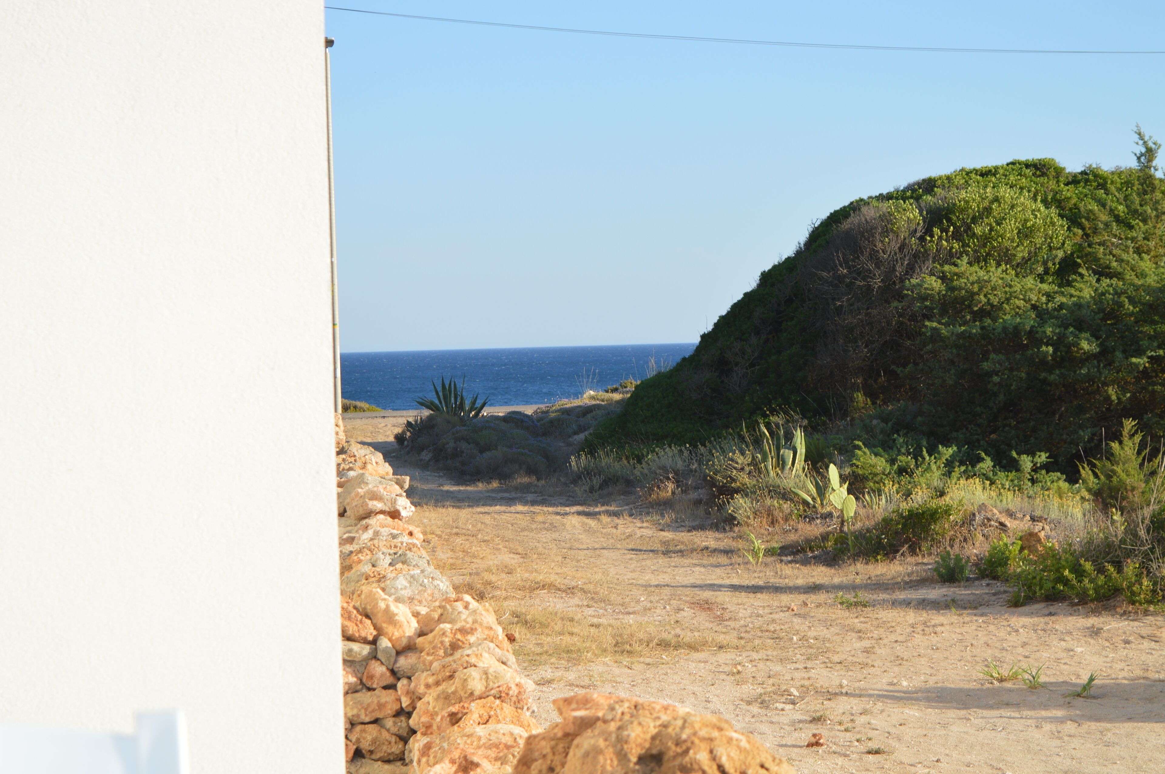 A coastal landscape with a stone wall, a rocky hill, and sparse vegetation.