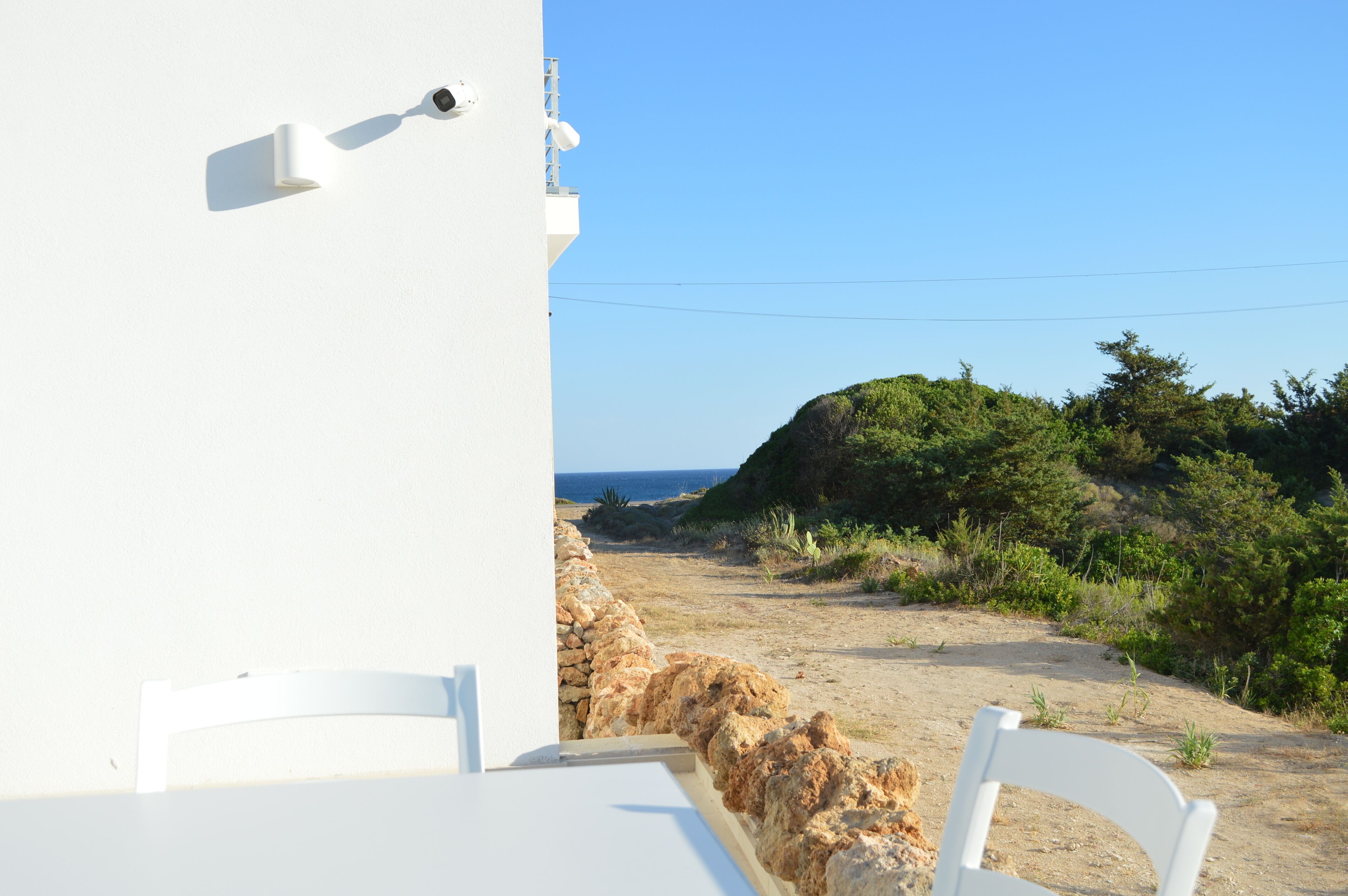 Ein weißes Gebäude mit einer Steinwand und Blick auf das Meer.