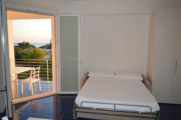 A bedroom with a bed, a sliding glass door leading to a balcony, and a view of the sea.