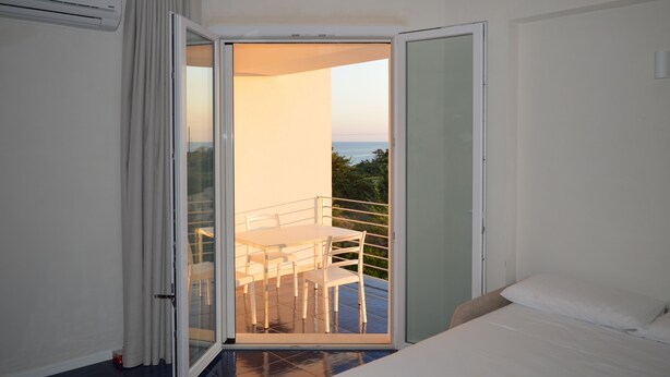 A room with a bed, a sliding glass door leading to an outdoor balcony with a table and chairs. - Myrtle studio apartment with sea view terrace, in the dunes 20m from free beach (Monaco Mirante)