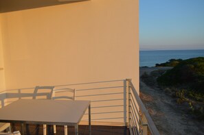A balcony with a table and chairs overlooking a beach.