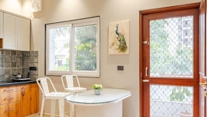 Una cocina con una mesa redonda, dos sillas blancas, una ventana y una puerta con mosquitero.