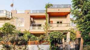 Un edificio moderno de dos plantas con techo plano, un balcón en el piso superior y una entrada protegida por una reja.