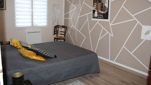 Un dormitorio con cama, una silla, un ventanal con persianas y una pared con diseños geométricos.