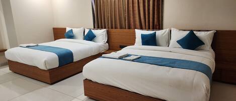 A hotel room with two single beds, each with a wooden headboard, white bedding, and blue accents.
