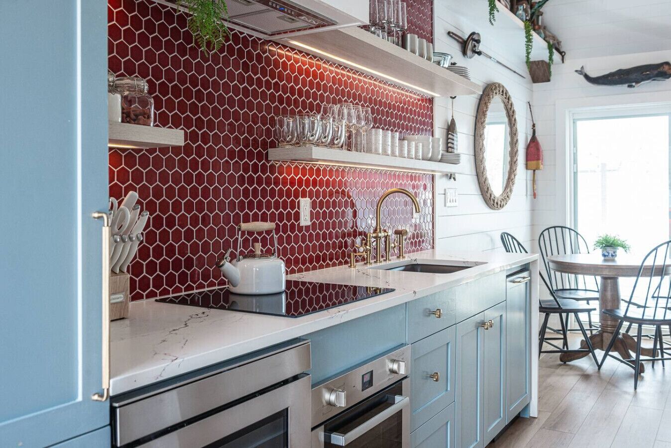 A modern kitchen with a red hexagonal backsplash, stainless steel appliances, and a dining area with a round table and chairs.