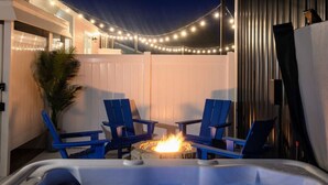 Un bain à remous avec deux chaises bleues, un foyer, des guirlandes lumineuses et une clôture blanche.