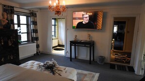 Une chambre à coucher comprenant un lit, un téléviseur, un lustre et une petite table sur laquelle sont posés des bustes.