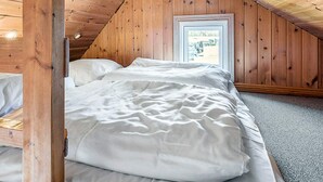 Une chambre avec un plafond en pente, des murs en bois, un lit avec une literie blanche et une fenêtre donnant sur l’extérieur.