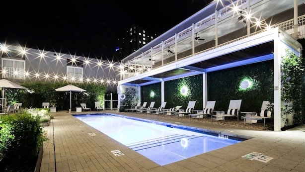A nighttime swimming pool area with lounge chairs and umbrellas, surrounded by greenery and illuminated by star-shaped lights. - Boutique Hotel with a Touch of History & Pool - Near Capitol Building (Austin)
