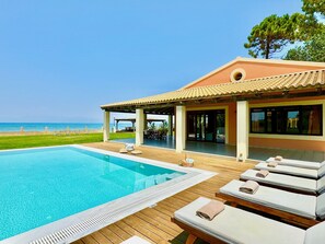 A poolside area with lounge chairs, a swimming pool, and a view of the beach.