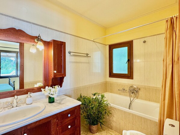 A bathroom with a wooden vanity, a bathtub, a window, and a potted plant.