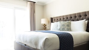 A neatly made bed with a tufted headboard, a bedside lamp, and a window with curtains.