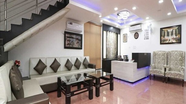 A modern living room with a staircase, a reception desk, and a sofa with cushions. - Hotel Max INN (Bhagalpur)