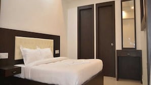 A bedroom with a bed, a nightstand, a dresser, a mirror, and two doors. - Hotel Max INN (Bhagalpur)