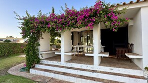 A covered outdoor seating area with white columns, a pergola with pink flowers, and a view of the interior. - Gemini by Check-in Portugal (Albufeira)