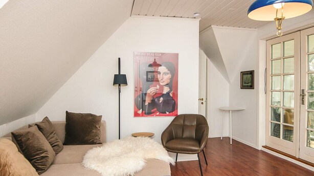 A modern living room with a high ceiling, a large poster on the wall, a brown leather chair, a beige sofa with multiple cushions, a fluffy white throw, and a black coffee table. - 2 Person Holiday Park Home in Fano (Fano)