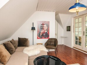 Un soggiorno moderno con soffitto alto, un grande quadro appeso al muro, una poltrona in pelle marrone, un divano beige con numerosi cuscini, una coperta bianca e soffice e un tavolino da caffè nero.