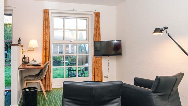 Une pièce avec un téléviseur fixé au mur, un bureau avec une lampe, deux chaises et une fenêtre avec des rideaux.