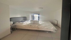 A small, clean room with a single bed, a bedside table, a window with bars, and a radiator. - Elegant Appt - 3BDR/8P - Near Paris & La Défense (Suresnes)