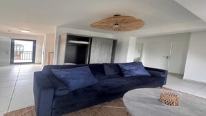 A modern living room with a dark blue sofa, a round coffee table, and a woven ceiling light fixture. - Elegant Appt - 3BDR/8P - Near Paris & La Défense (Suresnes)