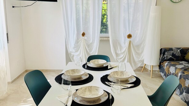 A dining area with a table set for four, chairs, a television mounted on the wall, and a window with curtains. - Modern three-room apartment with parking near the tower (Pisa)