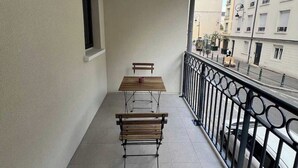 Un balcón con dos bancos de madera, una mesa pequeña y un ventanal.