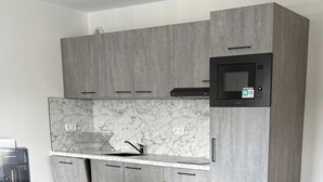 Una cocina moderna con armarios grises, salpicadero de mármol y microondas integrado.