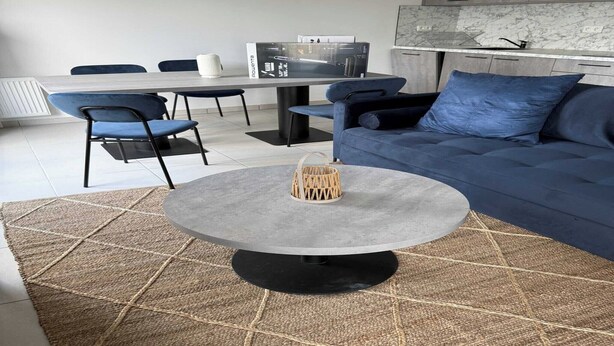 Una sala moderna con una mesa redonda, un sofá azul y sillas a juego. Se ve una mesa de comedor con sillas al fondo.