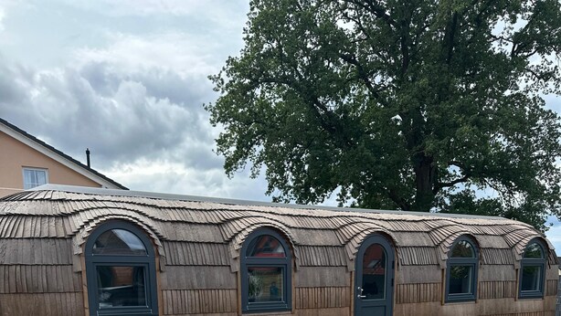 Ein holzhüttenartiges Gebäude mit Rundbogenfenstern und einer Badewanne im Vordergrund.