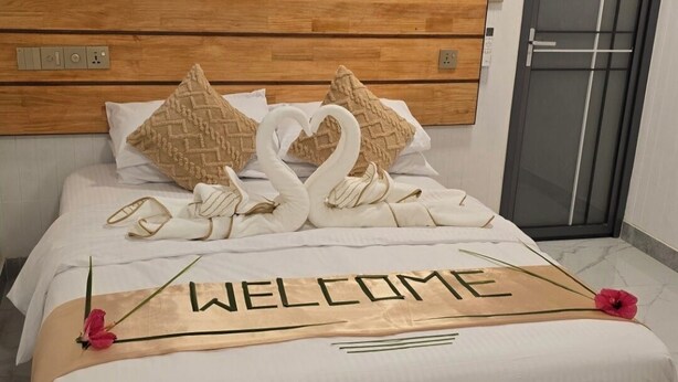 A neatly made bed with a 'WELCOME' sign, pillows, and a flower on a wooden headboard. - Charming 2-bedroom bed & breakfast in lovely Felidhoo with AC (Felidhoo)