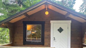 Eine Holzhütte mit einem großen Fenster und einer weißen Tür mit einem rautenförmigen Fenster.