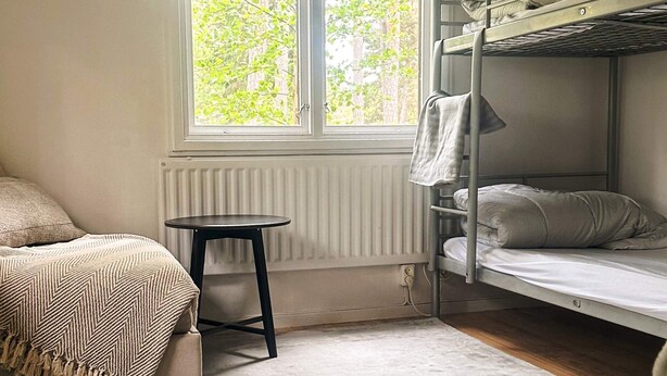 Ein Schlafraum mit Etagenbetten, einem Fenster, einem kleinen Tisch und einem Bett mit gemustertem Überwurf.