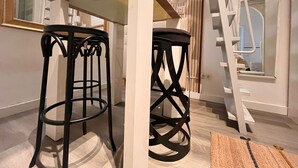 A room with a wooden floor, two black stools, a white table, a mirror, and a ladder leaning against the wall. - Charming apartment for seasonal rental (Madrid)