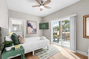 Una camera da letto con un letto, un comodino verde, una ventola a soffitto, un'ampia finestra e una porta scorrevole in vetro che dà su una zona esterna.
