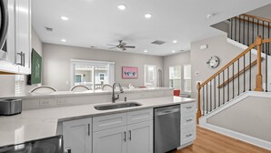Una cocina moderna con lavavajillas integrado, armarios blancos, una campana de acero inoxidable y una escalera de madera.