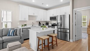 Una cocina moderna con armarios blancos, electrodomésticos de acero inoxidable y una isla central con taburetes.