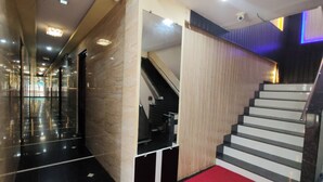 A modern hotel lobby with a red carpet, a staircase, and a glass elevator. - Hotel Sai Samrat Inn (Panvel)