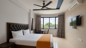 A hotel room with a bed, a desk, a chair, a TV, and a window with curtains. - Hotel Sai Samrat Inn (Panvel)