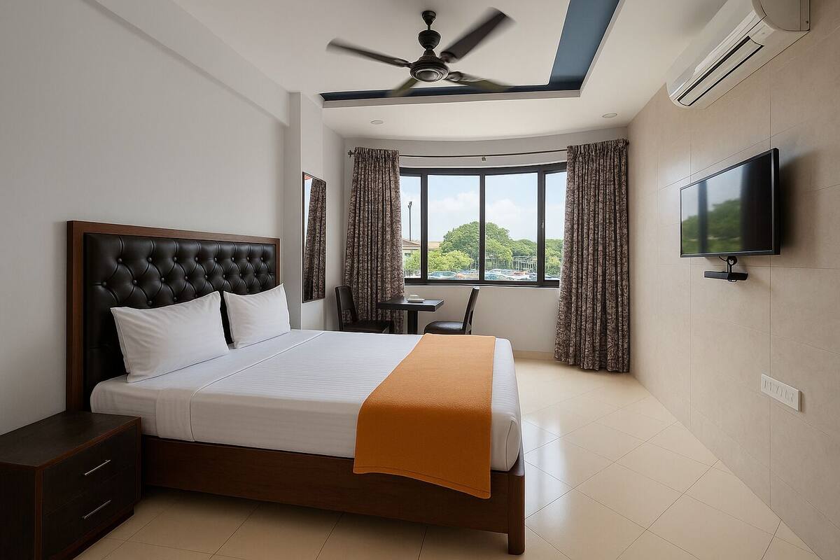 A hotel room with a bed, a desk, a chair, a TV, and a window with curtains.
