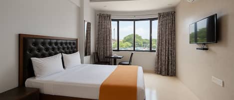 A hotel room with a bed, a desk, a chair, a TV, and a window with curtains.