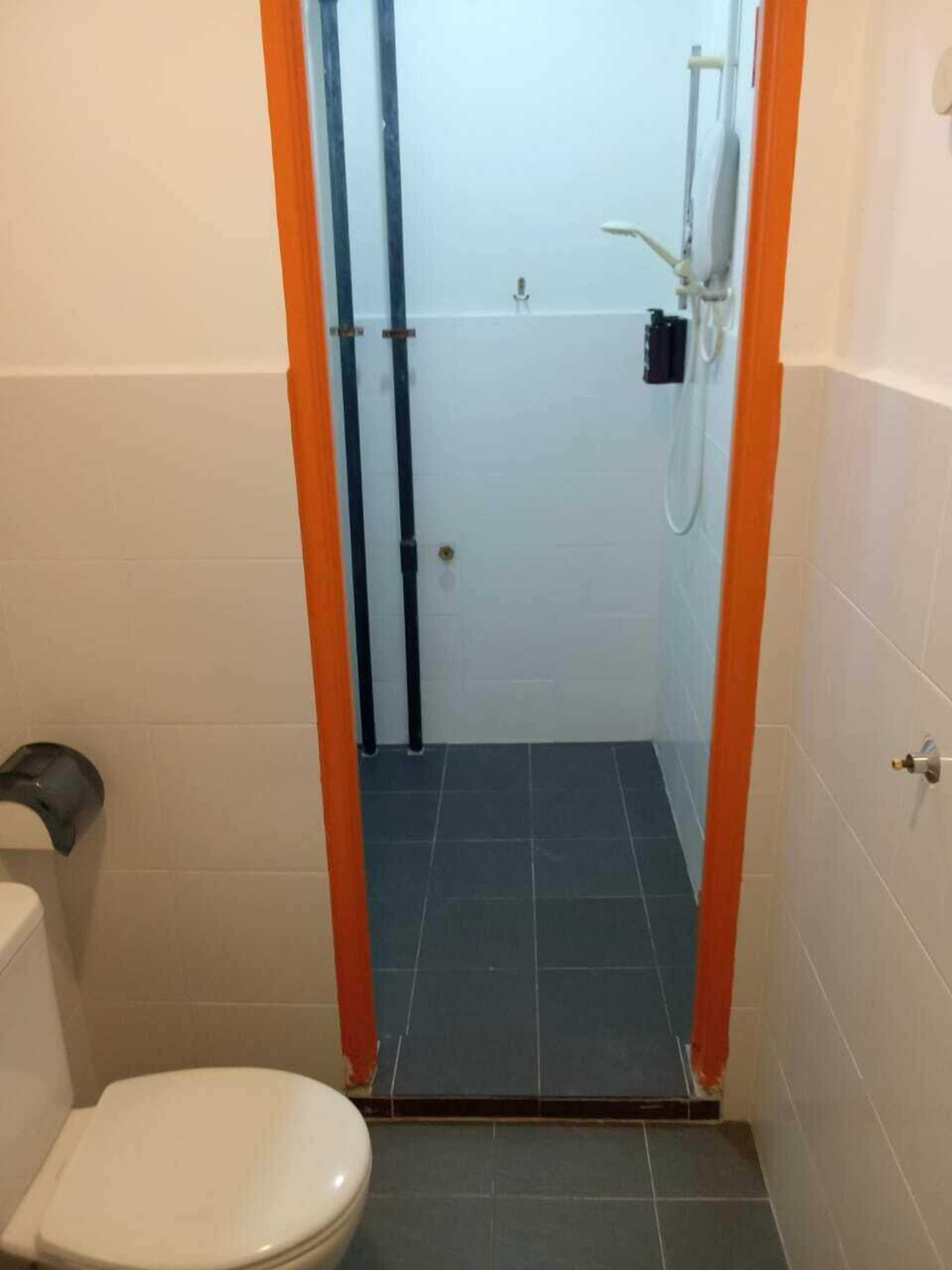A small bathroom with a toilet, a shower, and a door leading to a larger room.