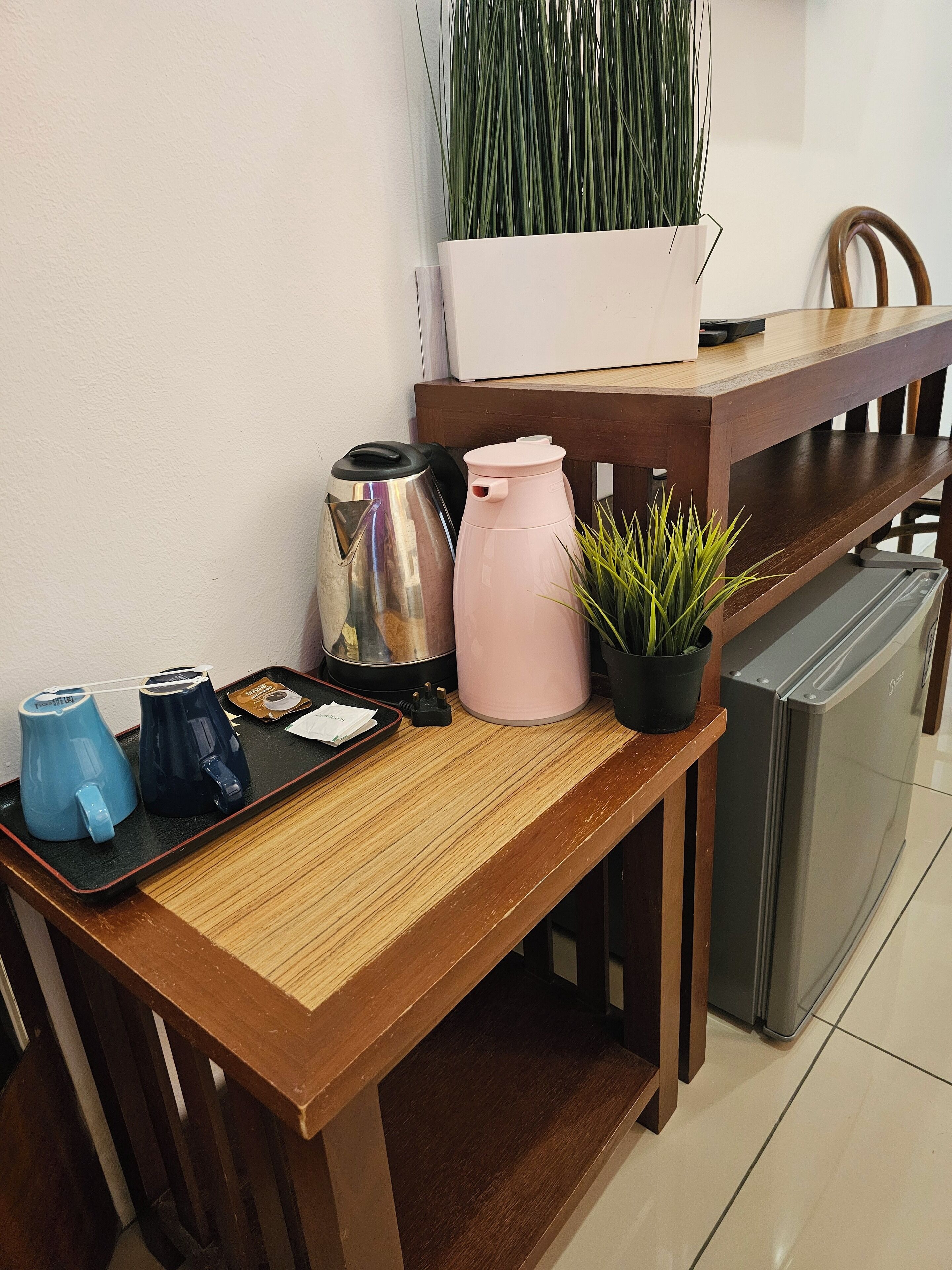 A kitchen counter with a coffee maker, a kettle, a thermos, a small potted plant, and a refrigerator.